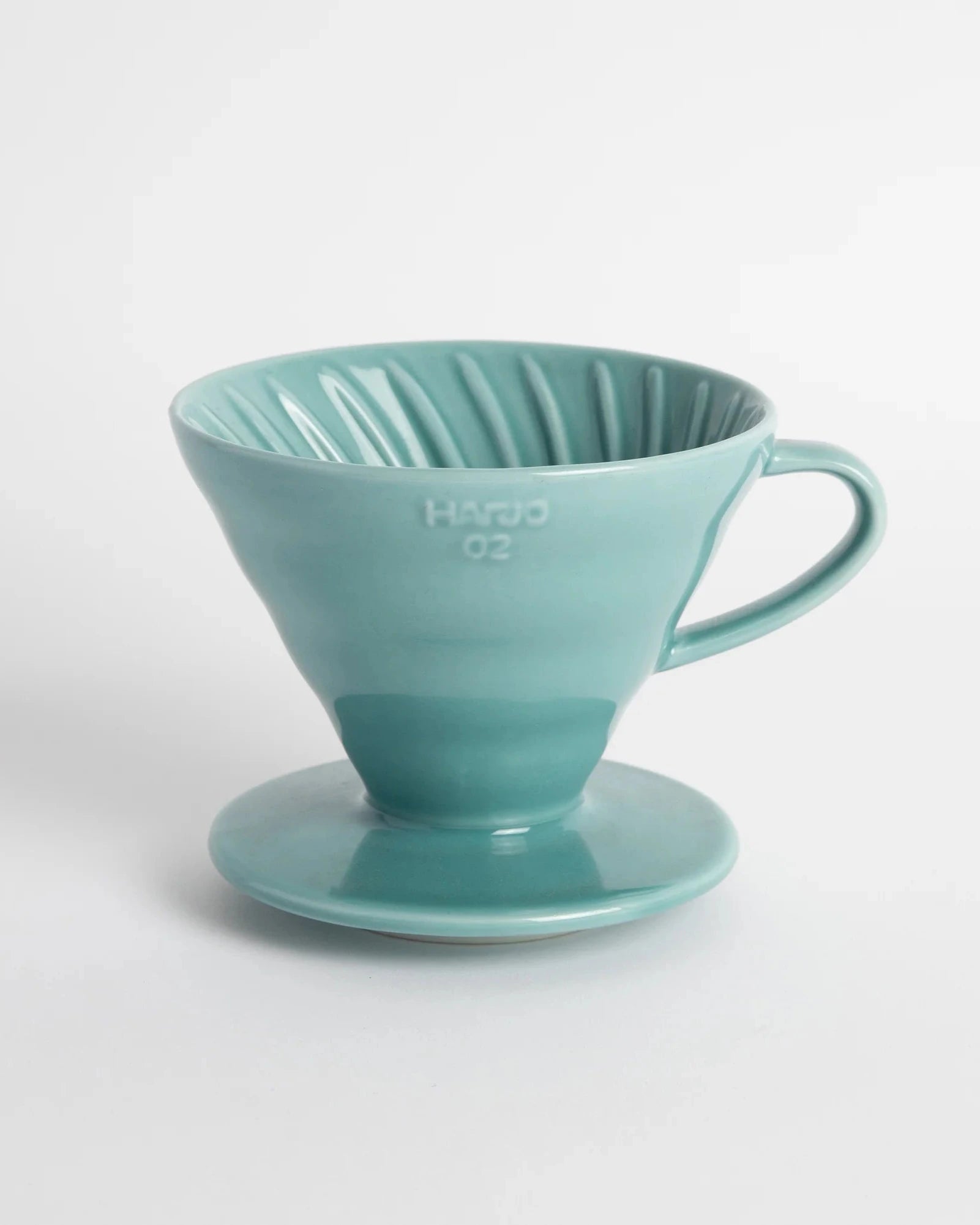 A turquoise Hario V60-02 ceramic coffee dripper with a paper filter, placed on a white surface.
