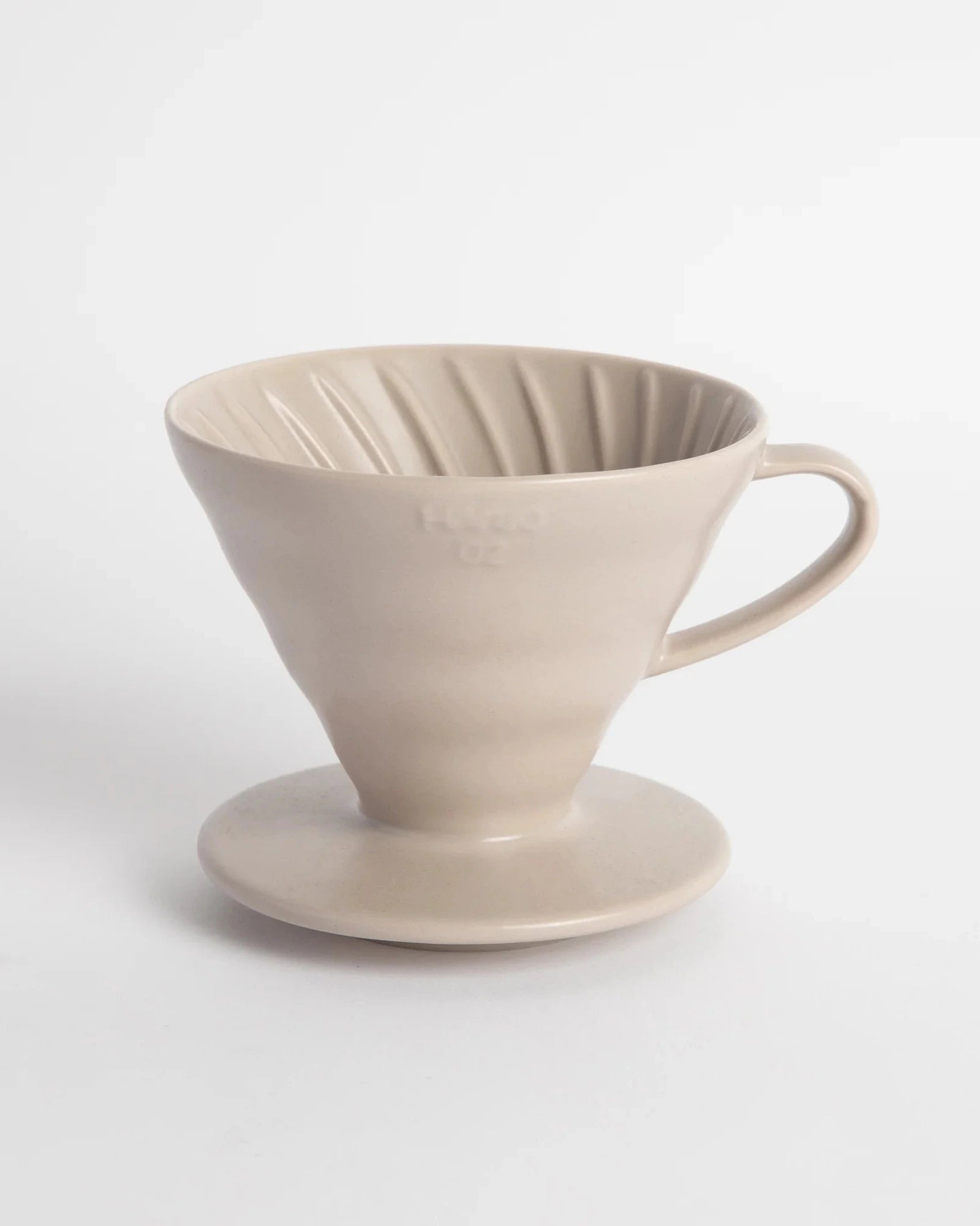 A beige Hario V60-02 ceramic coffee dripper with a cone shape and a handle on top, placed on a white background.